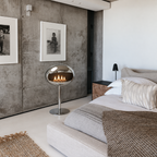 Cheminée éthanol sur pied chrome pour chambre design, mur en béton brut et photographies encadrées