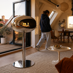 Poêle éthanol chrome allumé dans un salon sous combles ouvert sur une terrasse au coucher du soleil