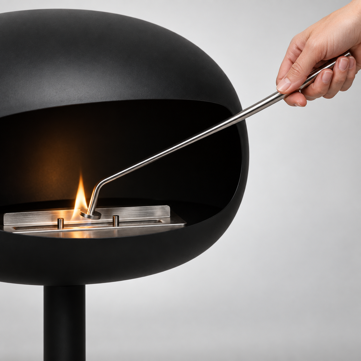 Main allumant le brûleur d'une cheminée éthanol noire avec l'outil d'allumage Maison Flamme